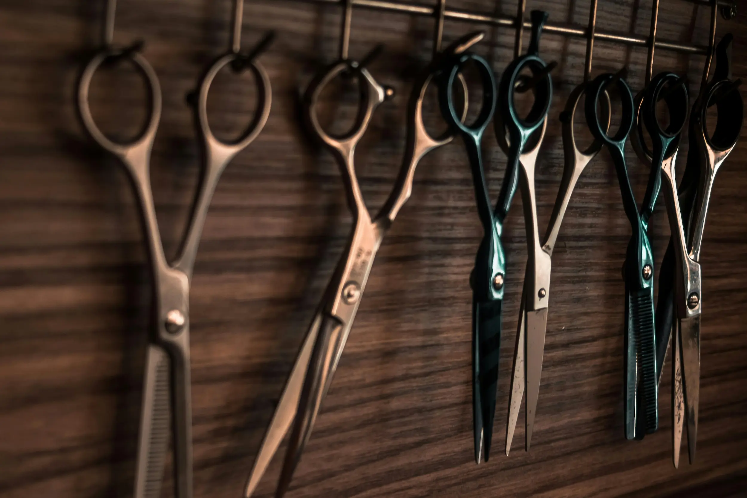 Barber shears and thinning scissors hanging in a row against a wooden wall